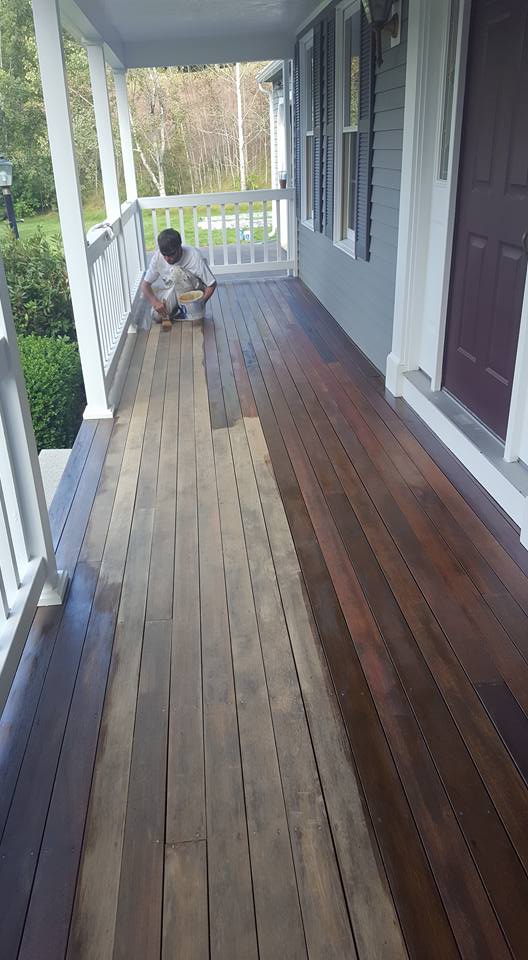 Painter applying fresh coat of stain to porch
